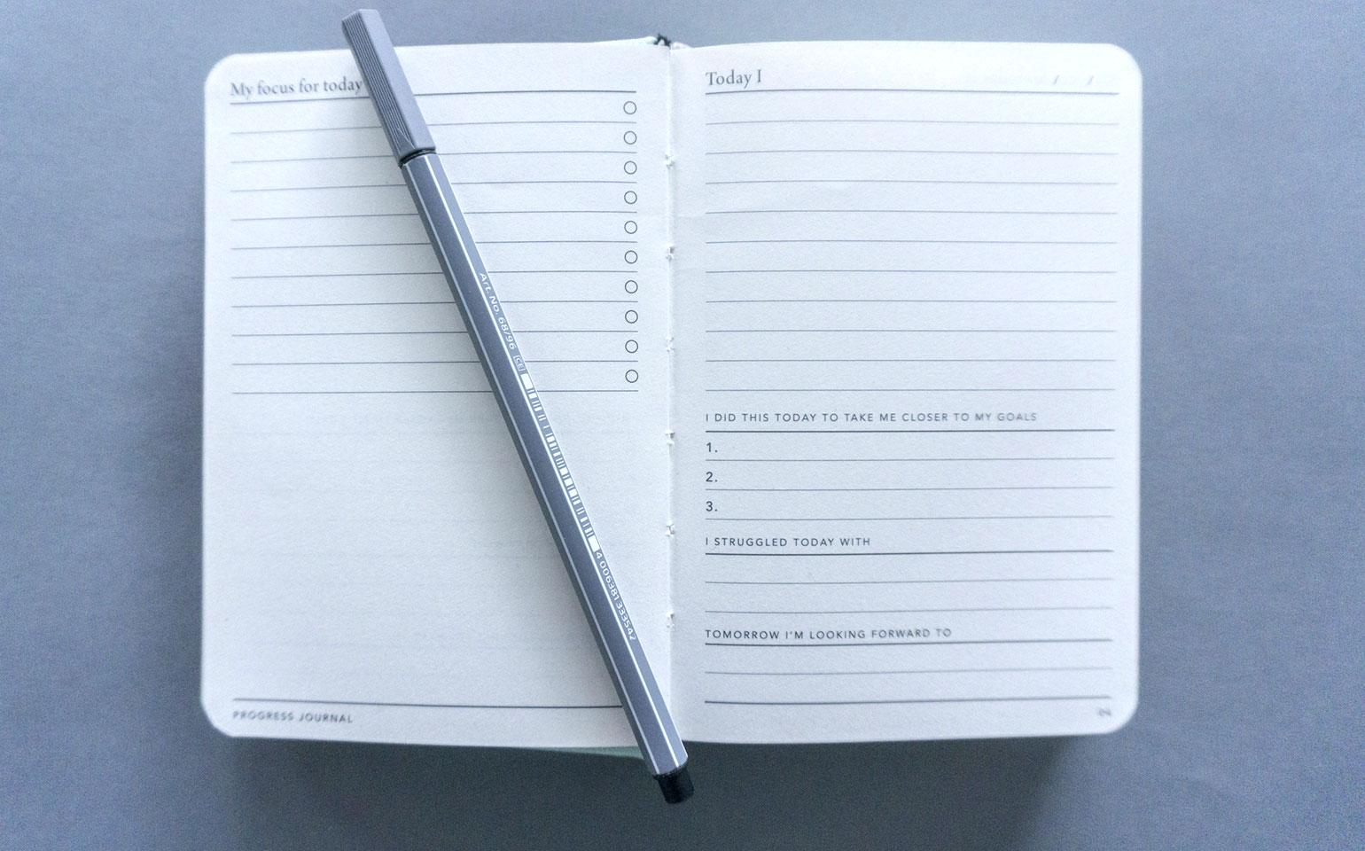 A journal is shown open to a blank page with a pen resting on top of it.