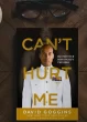 Overcoming emotional pain and resilience, "Can't Hurt Me" book by David Goggins on a wooden desk with a coffee cup, glasses, notebook, and pens, emphasizing mental toughness, personal development, and self-help.